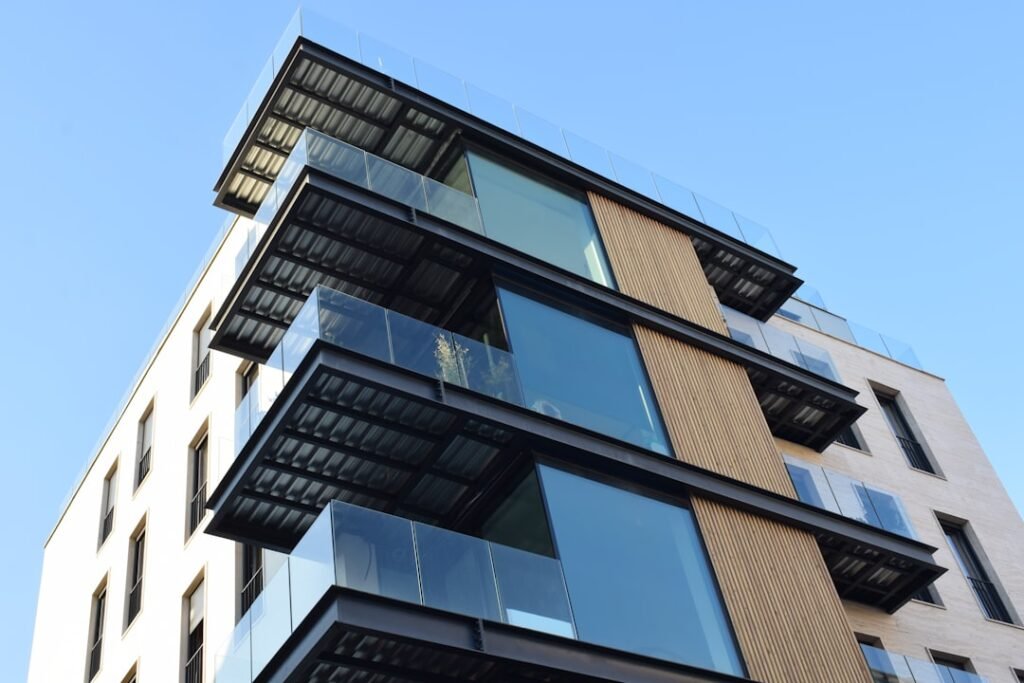Edificio moderno de varias plantas con terrazas cerradas con vidrio y estructura de aluminio oscuro, vista desde abajo