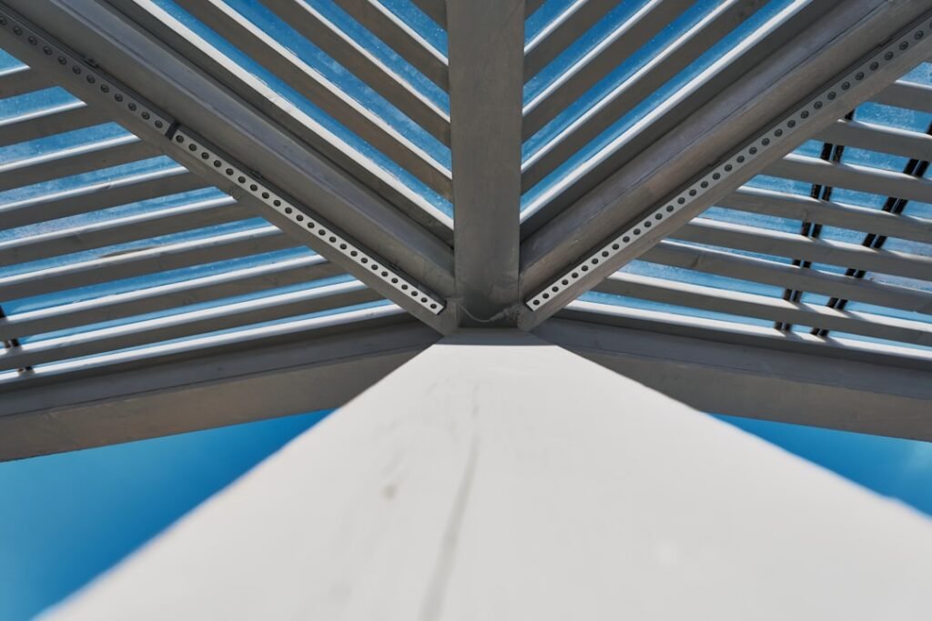 Detalle de lamas de aluminio orientables en una pérgola bioclimática vistas desde abajo contra el cielo azul