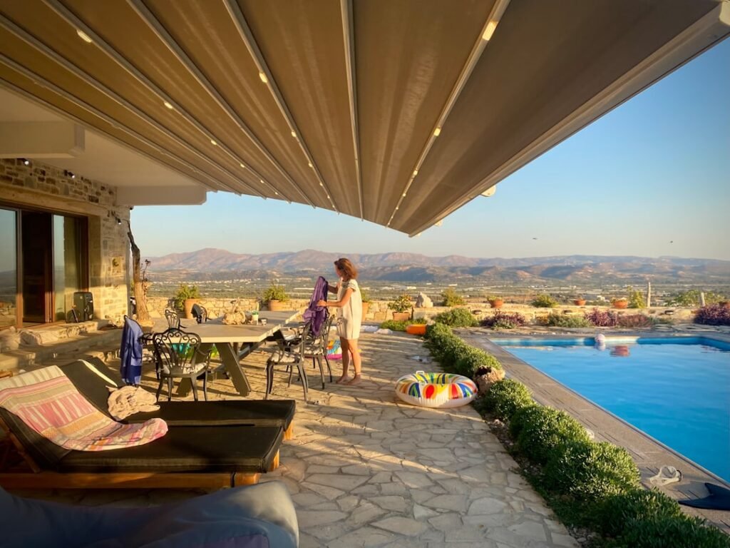 Pérgola con lamas orientables sobre terraza de piedra junto a piscina exterior, regulando sombra y ventilación en verano