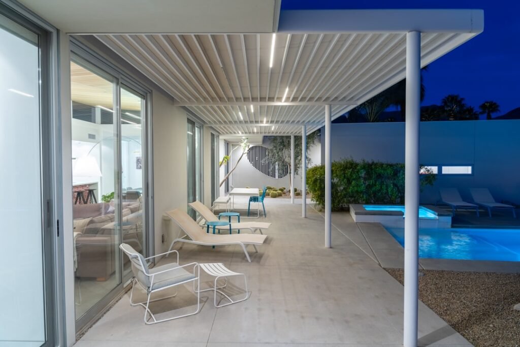 Pérgola bioclimática de lamas de aluminio blanco sobre terraza exterior con tumbonas y piscina, ejemplo de instalación residencial