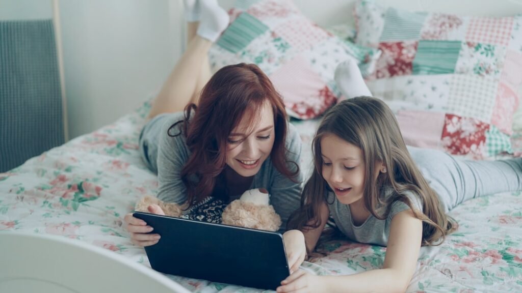 Mother and daughter smiling together while using a tablet at home