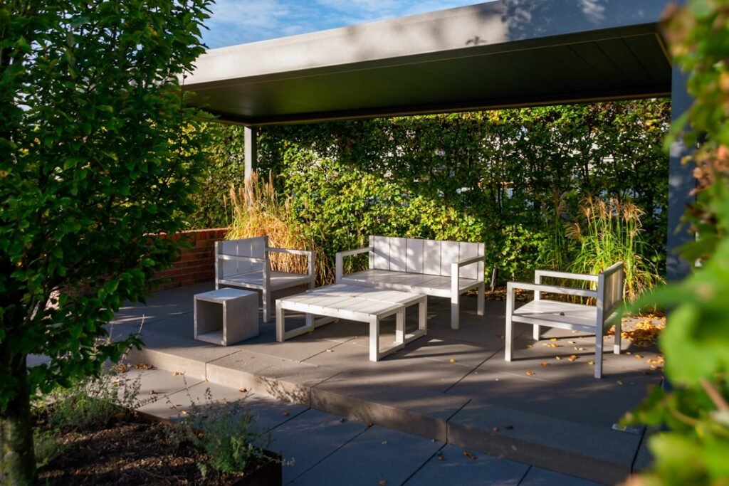 Zona de estar exterior con pérgola moderna, mobiliario blanco y jardín verde